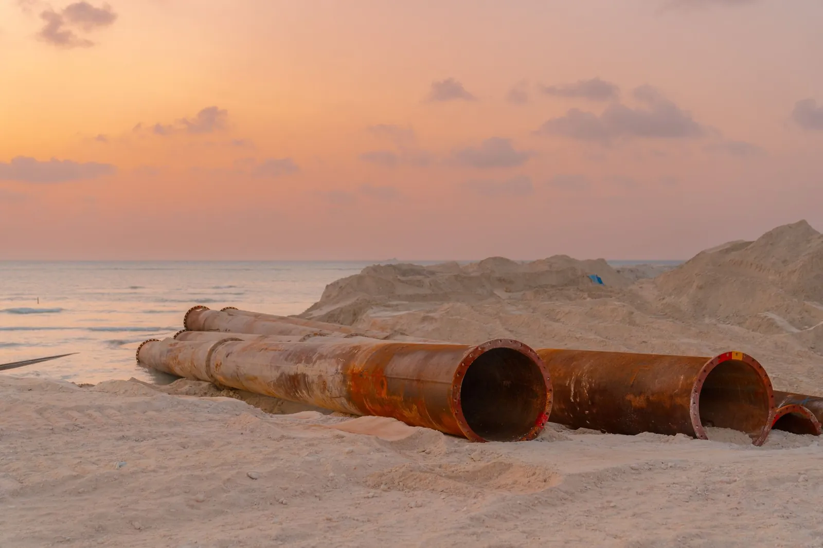 Rusty pipes at a coastal construction site with scenic sunset view. Stock photo illustrating Welspun Corp's new order story.