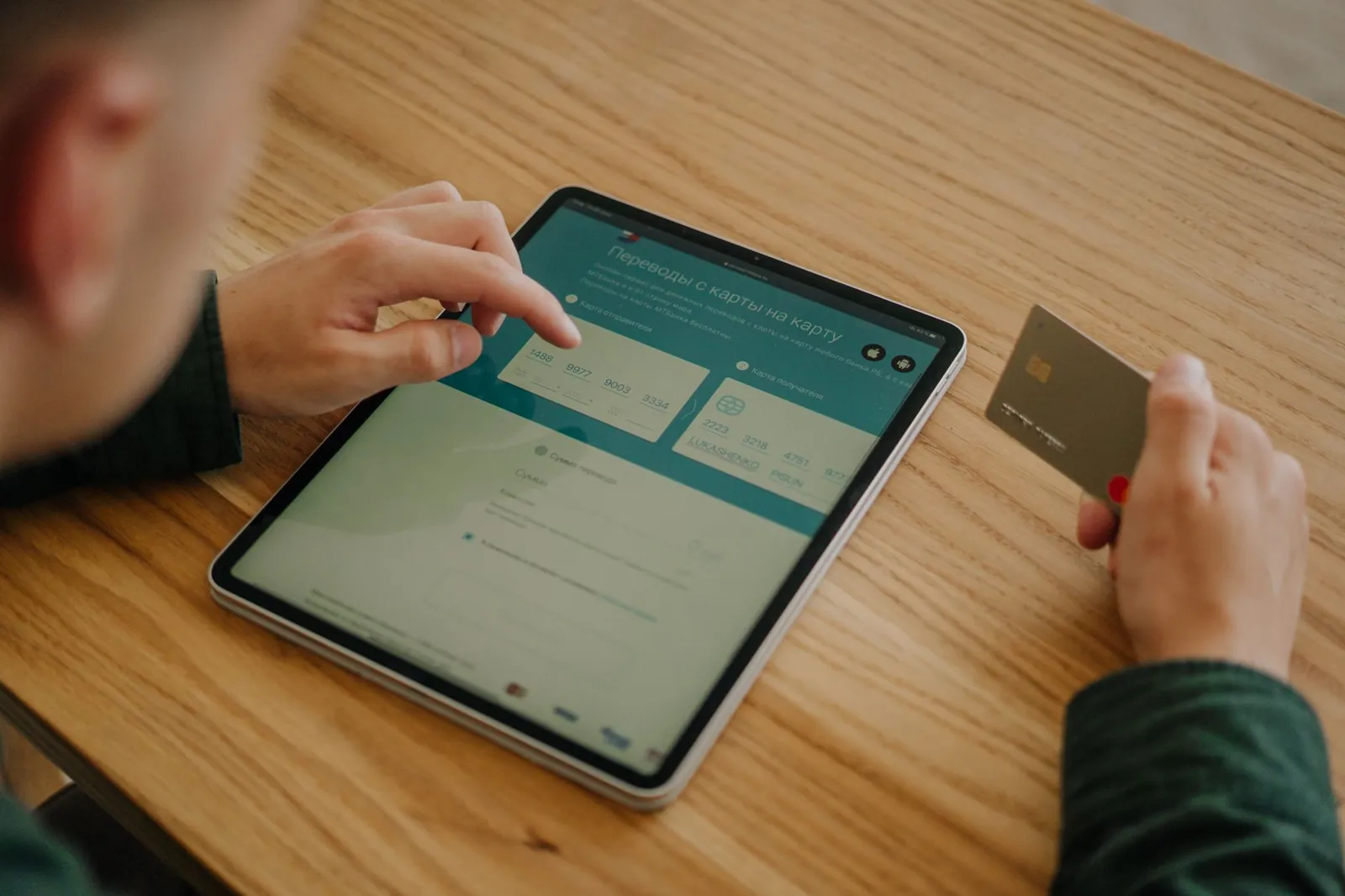 Person making an online payment using a tablet and credit card on a wooden desk. Stock photo illustrating Aurionpro Solutions' new order story.