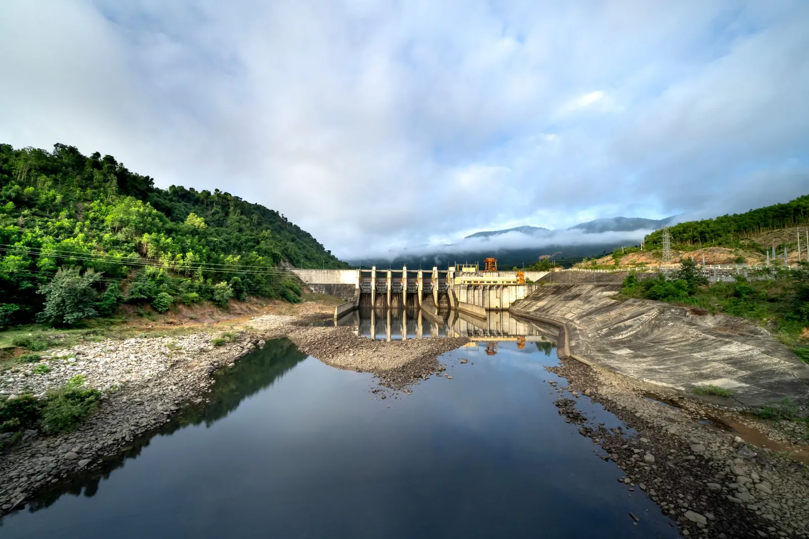 Hydroelectric power plant for production of eco friendly electricity on river flowing in green hilly valley. Stock photo illustrating Om Infra's new order story.