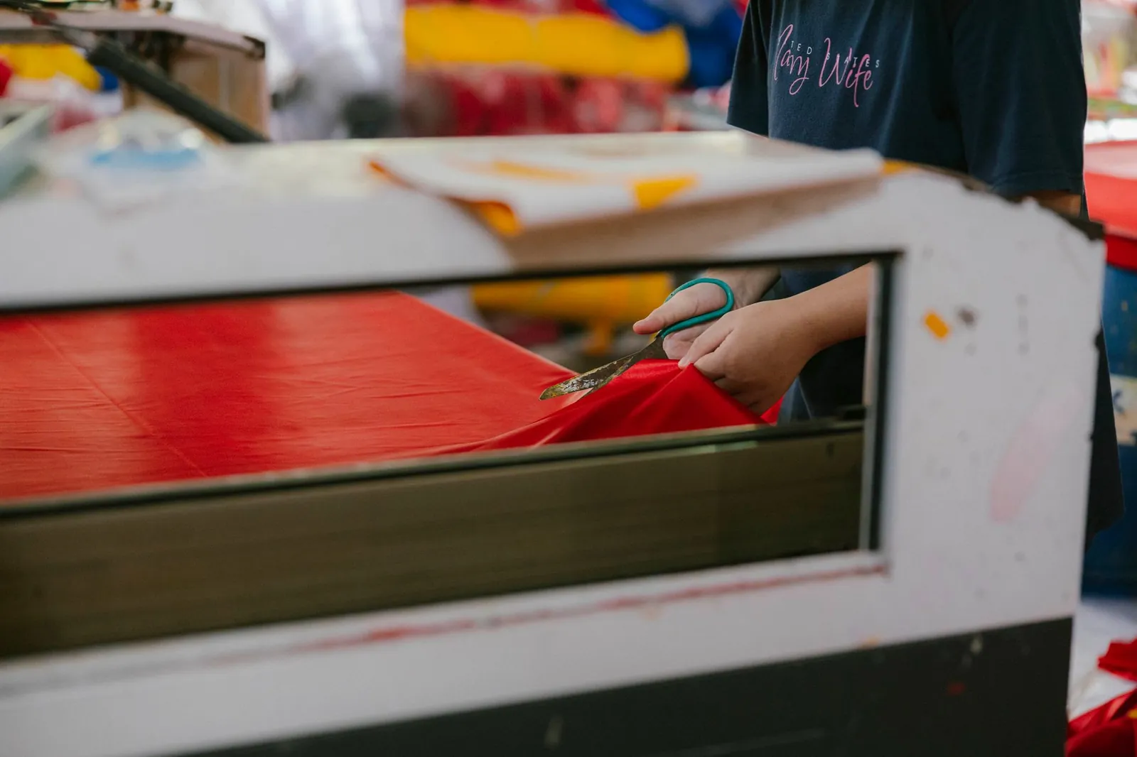 A factory worker precisely cuts red fabric with scissors, showcasing textile production. Stock photo illustrating Shanti Gold International's fund raise story.