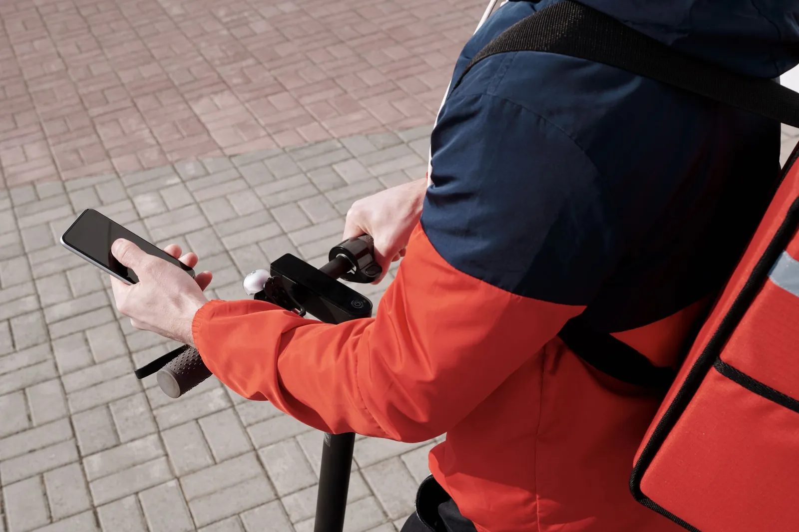 A delivery person riding an electric scooter using a smartphone for navigation outdoors. Stock photo illustrating BikeWo Green Tech's expansion story.