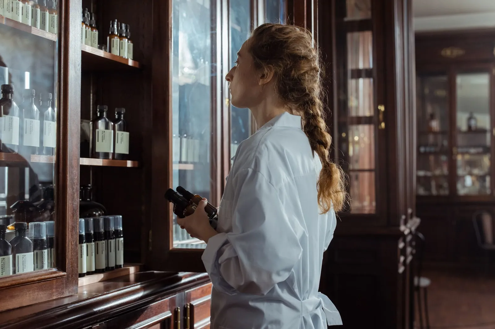 Woman in white coat examines medicine bottles in a vintage pharmacy setting. Stock photo illustrating Sat Kartar Life's fund raise story.