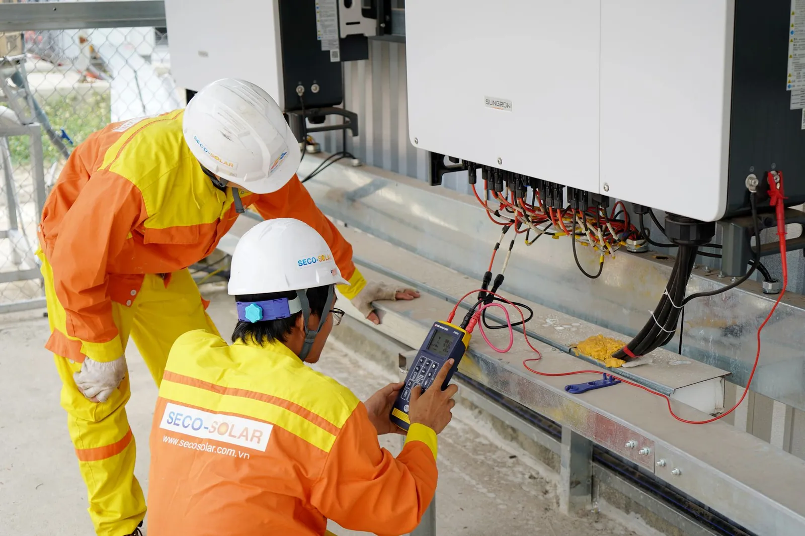 Two electrical engineers installing and testing solar power systems wearing safety gear at a construction site. Stock photo illustrating Nava's production started story.