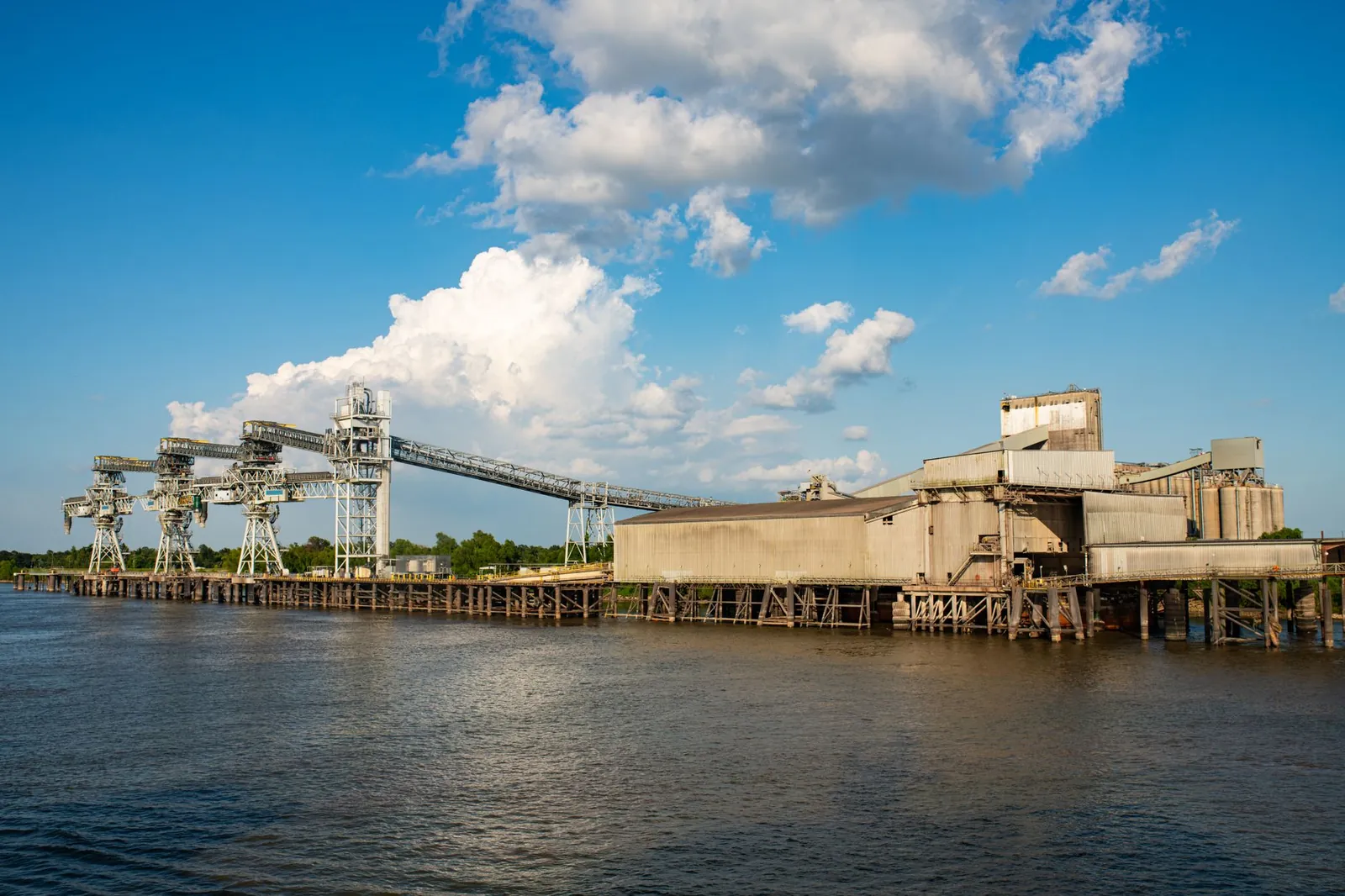 An extensive industrial port facility on a riverside under a blue sky with clouds. Stock photo illustrating Beezaasan Explotech's fund raise story.