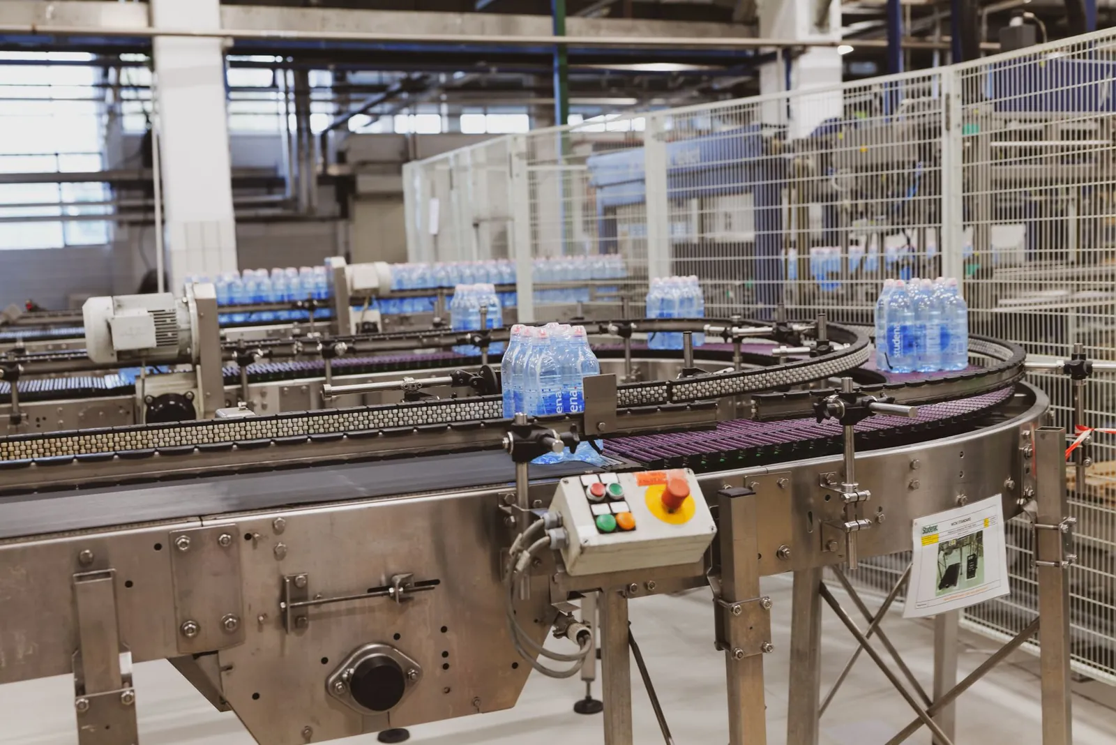 Water bottles being processed on an automated conveyor in a modern factory setting. Stock photo illustrating Shree Rama Multi-Tech's expansion story.