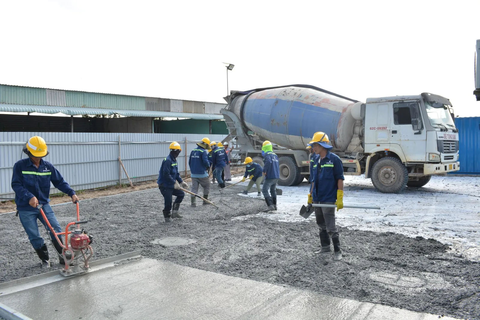 Workers in safety gear pouring concrete outdoors with a cement mixer truck. Stock photo illustrating Refex Industries' production started story.