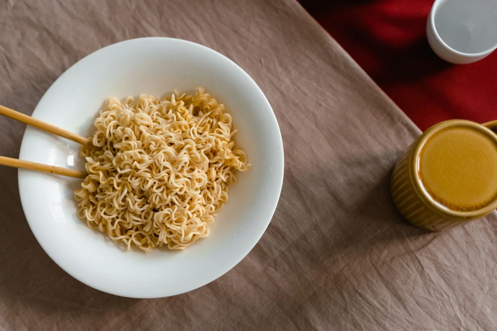 A delicious serving of instant noodles in a white bowl with chopsticks on a textured table. Stock photo illustrating NHC Foods' product launched story.