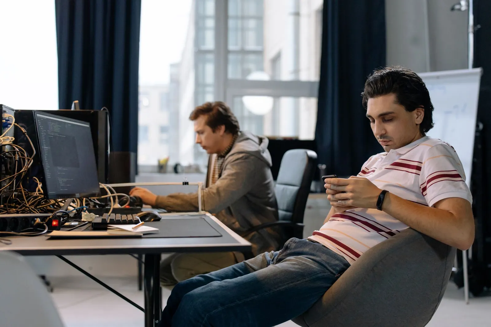 Two men working in a modern office, one on a computer and the other on a smartphone. Stock photo illustrating Happiest Minds Technologies' product launched story.
