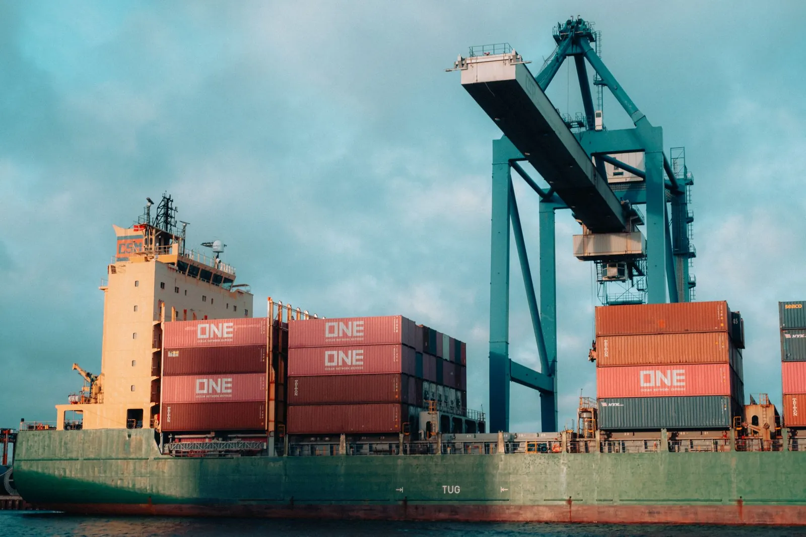 Large cargo ship loaded with colorful containers at a bustling industrial port. Stock photo illustrating JSW Infrastructure's production started story.
