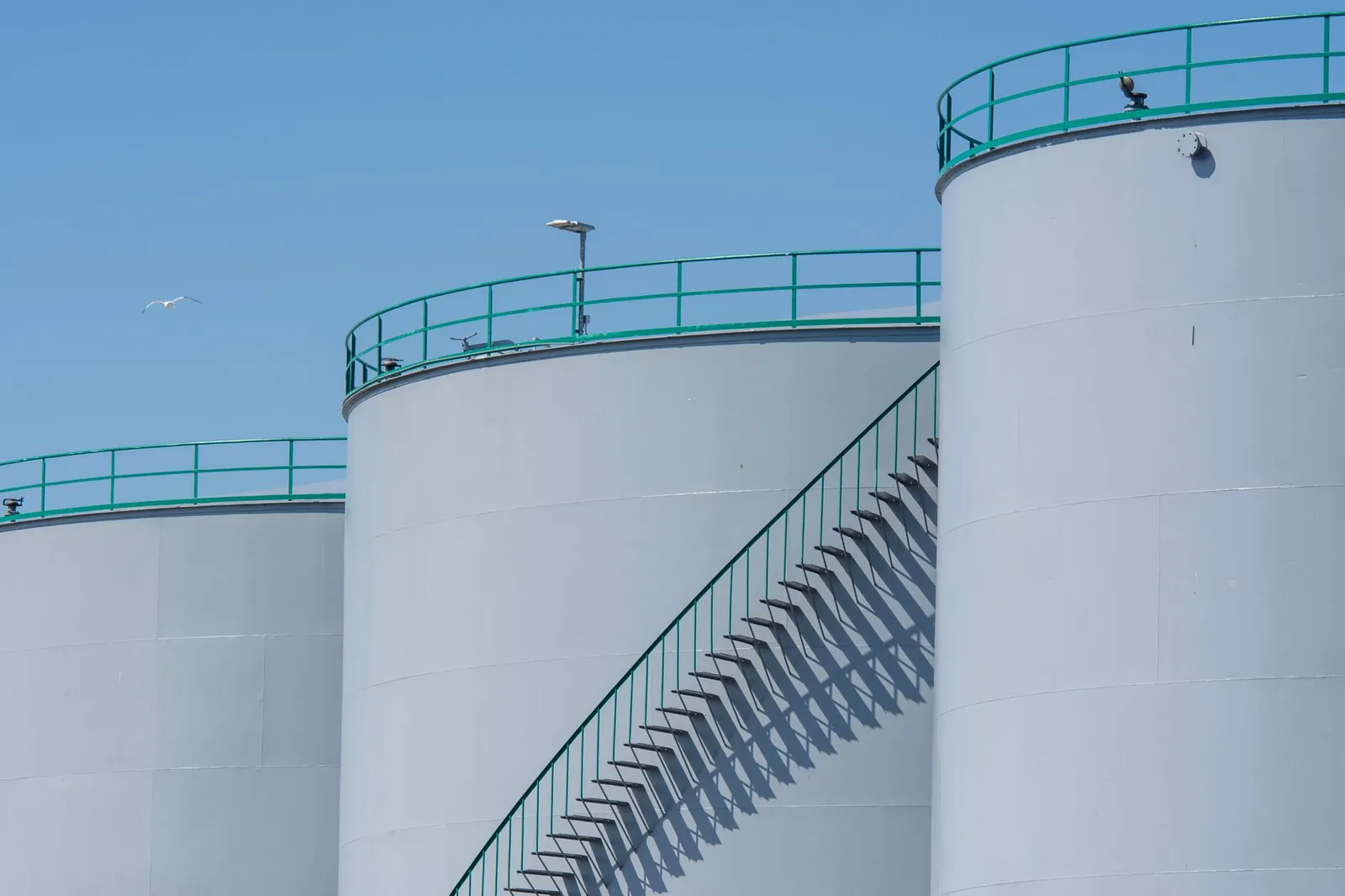Industrial storage tanks with metal stairways under a clear blue sky, highlighting industrial architecture. Stock photo illustrating ACME Solar Holdings' production started story.