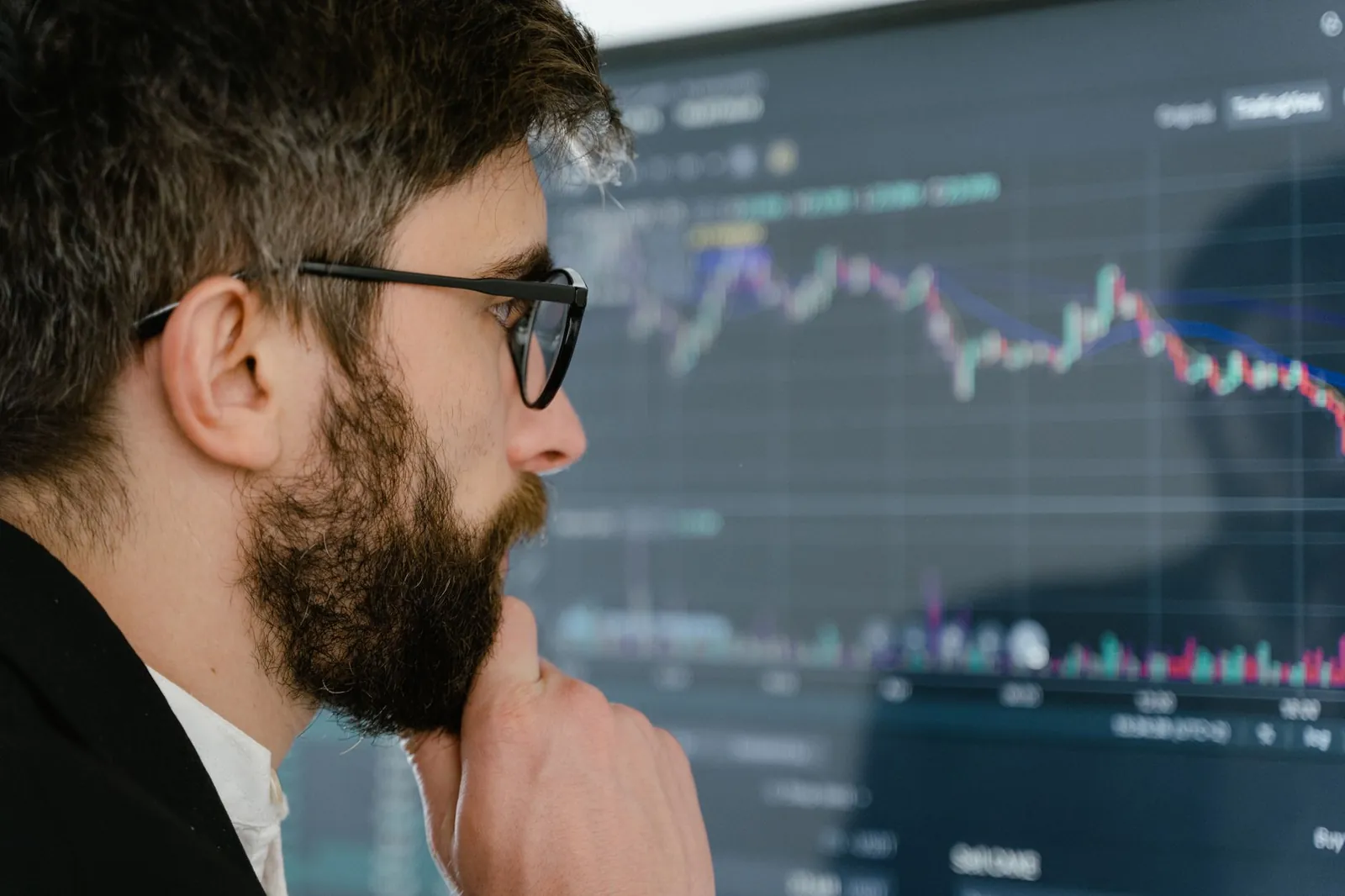 A focused man with glasses studies stock market graphs on a screen, pondering insights. Stock photo for the ALFA News guide: Auditor Resignation Disclosure: A SEBI Guide for Indian Investors.