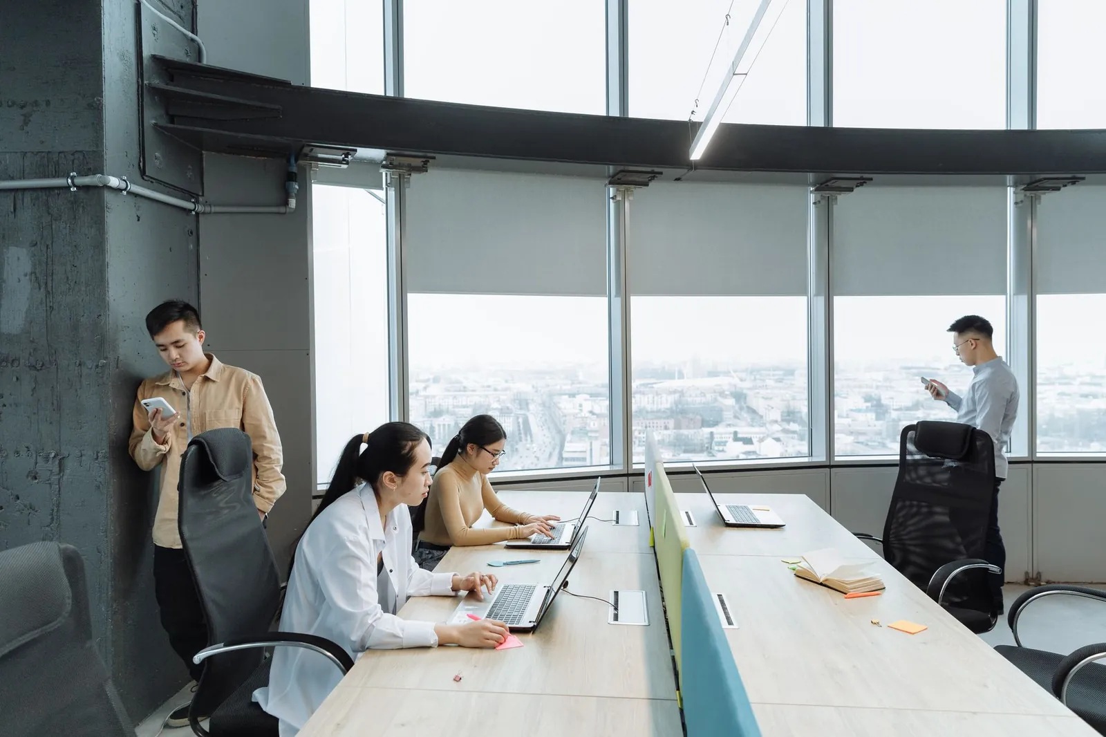 Contemporary office scene with Asian coworkers working on laptops and smartphones. Stock photo illustrating Indiqube Spaces' earning call story.