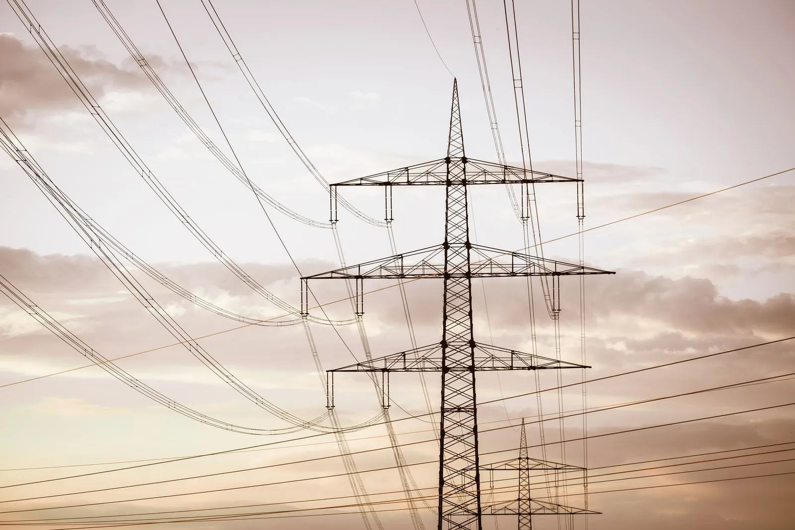 Silhouetted electricity pylons and power lines against a dramatic sky at sunset. Stock photo illustrating Adani Energy Solutions' fund raise story.