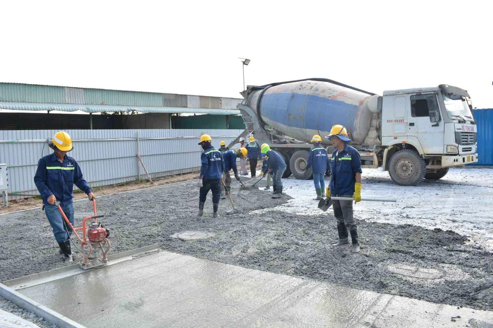 Team of workers pouring cement from a mixer truck on a construction site, ensuring proper leveling. Stock photo illustrating ArisInfra Solutions' promoter buying story.