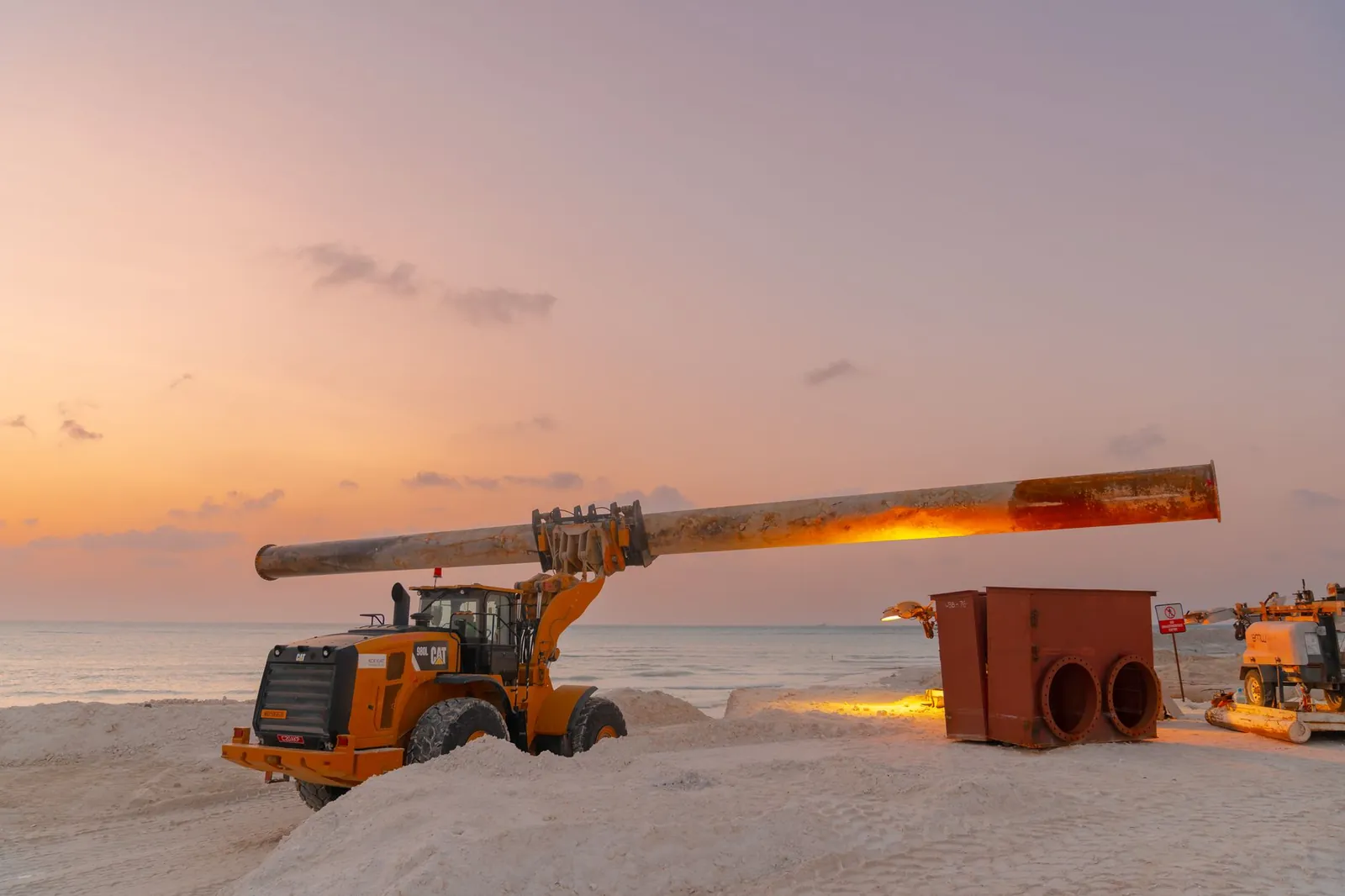 Dramatic view of beach construction site with heavy machinery at sunset. Stock photo illustrating Dilip Buildcon's new order story.
