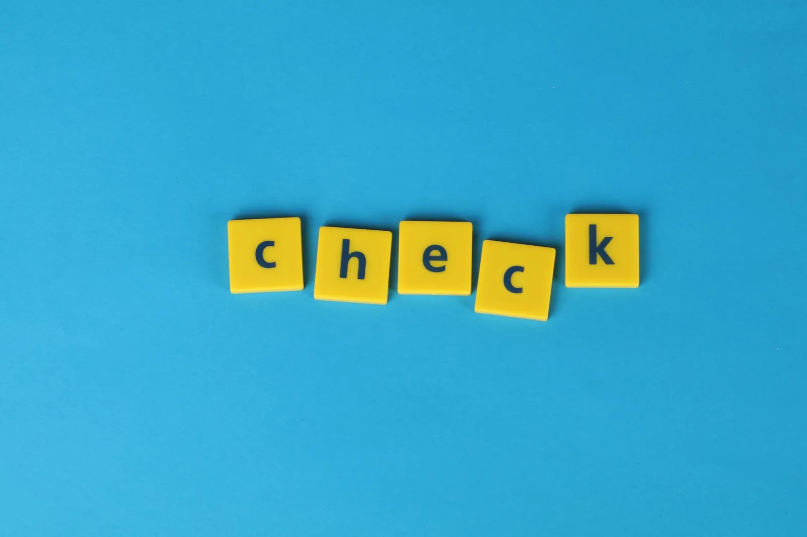 Yellow letter tiles spelling 'check' on a vibrant blue background, conveying approval or verification. Stock photo for the ALFA News guide: Rumour Verification Under SEBI Rules: A Guide for Investors.