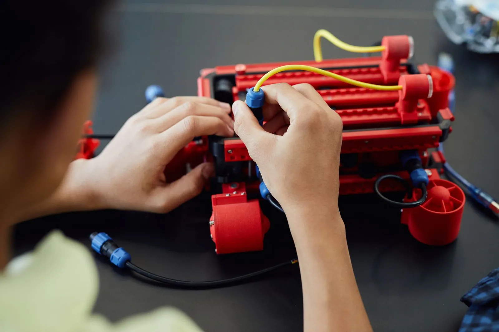 Close-up of hands assembling a robotic project with cables indoors, showcasing technology and electronics. Stock photo illustrating Craftsman Automation's fund raise story.