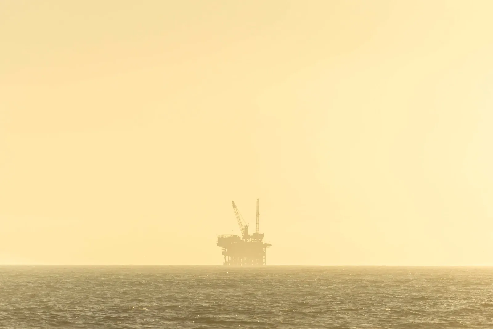 Distant view of an offshore oil platform against a golden sky at sunset over a calm sea. Stock photo illustrating Lakshya Powertech's new order story.