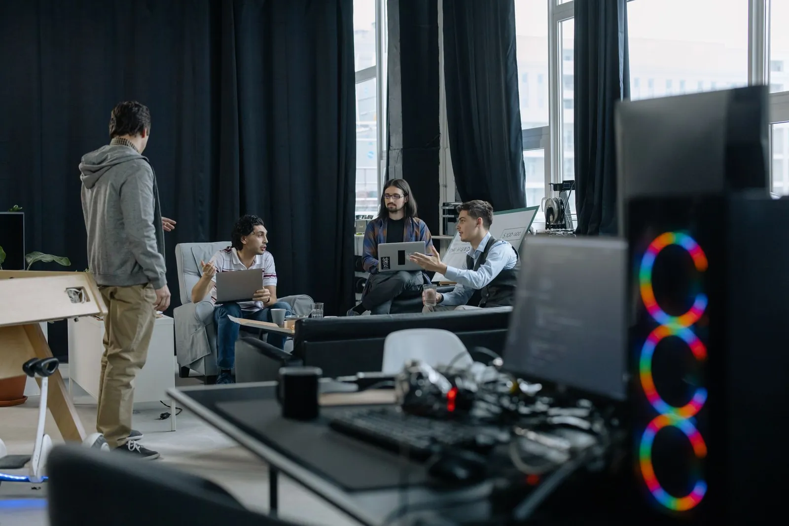 A group of professionals engaged in a casual meeting at a modern office, discussing projects on laptops and tablets. Stock photo illustrating ASM Technologies' fund raise story.