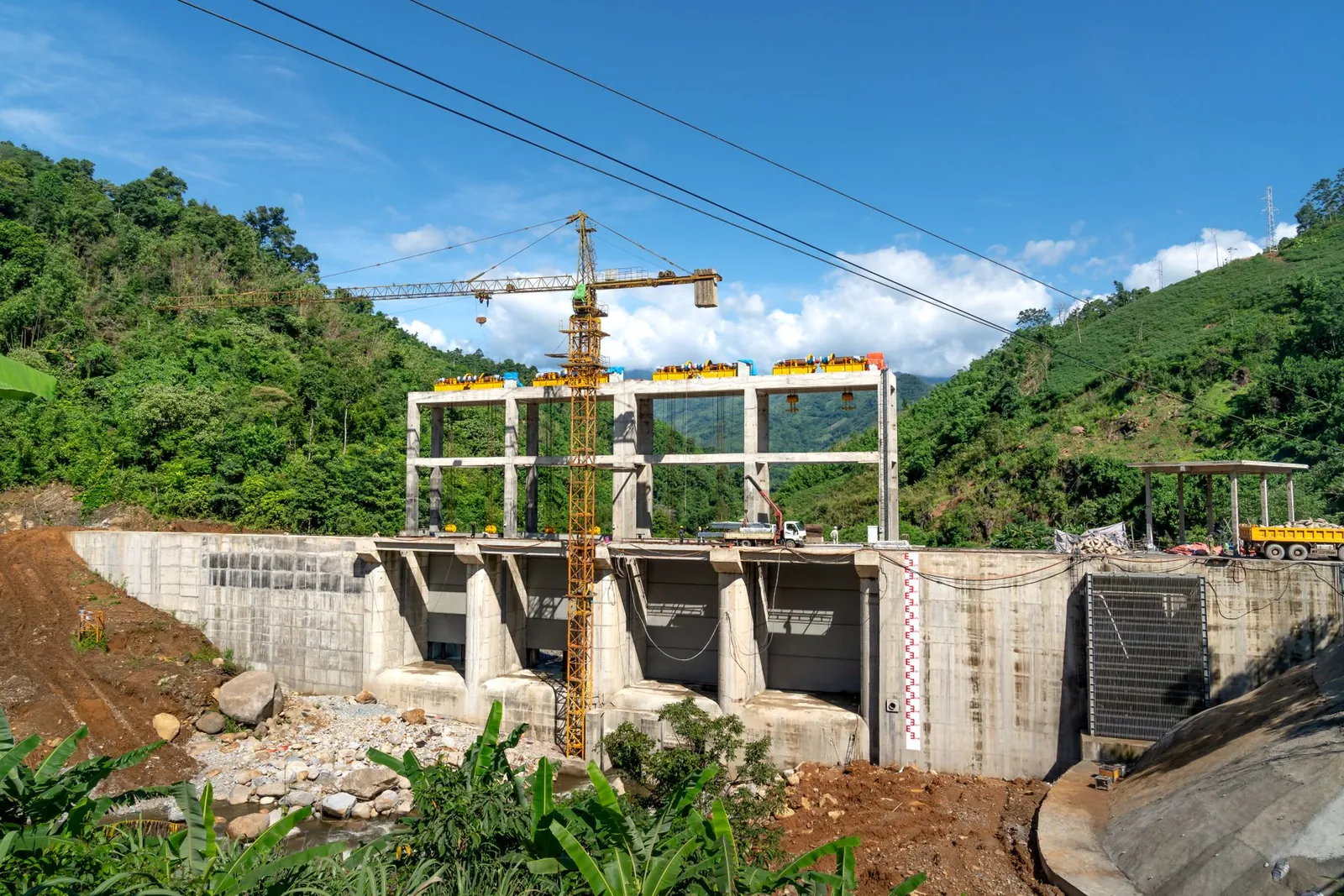 Crane operating at a construction site in a lush, mountainous area under bright blue skies. Stock photo illustrating DMR Engineering's new order story.