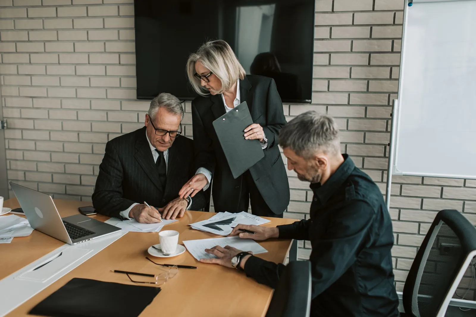 Three mature professionals in a business meeting discussing and signing documents in an office setting. Stock photo illustrating Jana Small Finance Bank's regulatory approval story.
