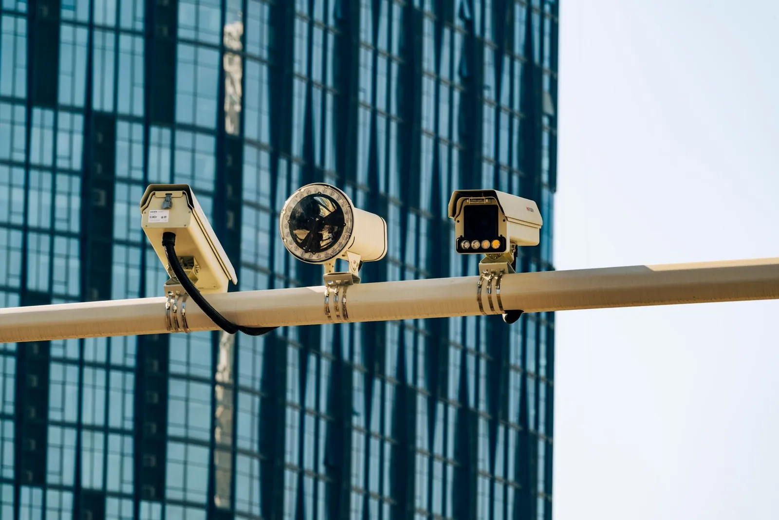 Surveillance cameras mounted on a pole in front of a modern glass building. Stock photo illustrating RRP Defense's product launched story.