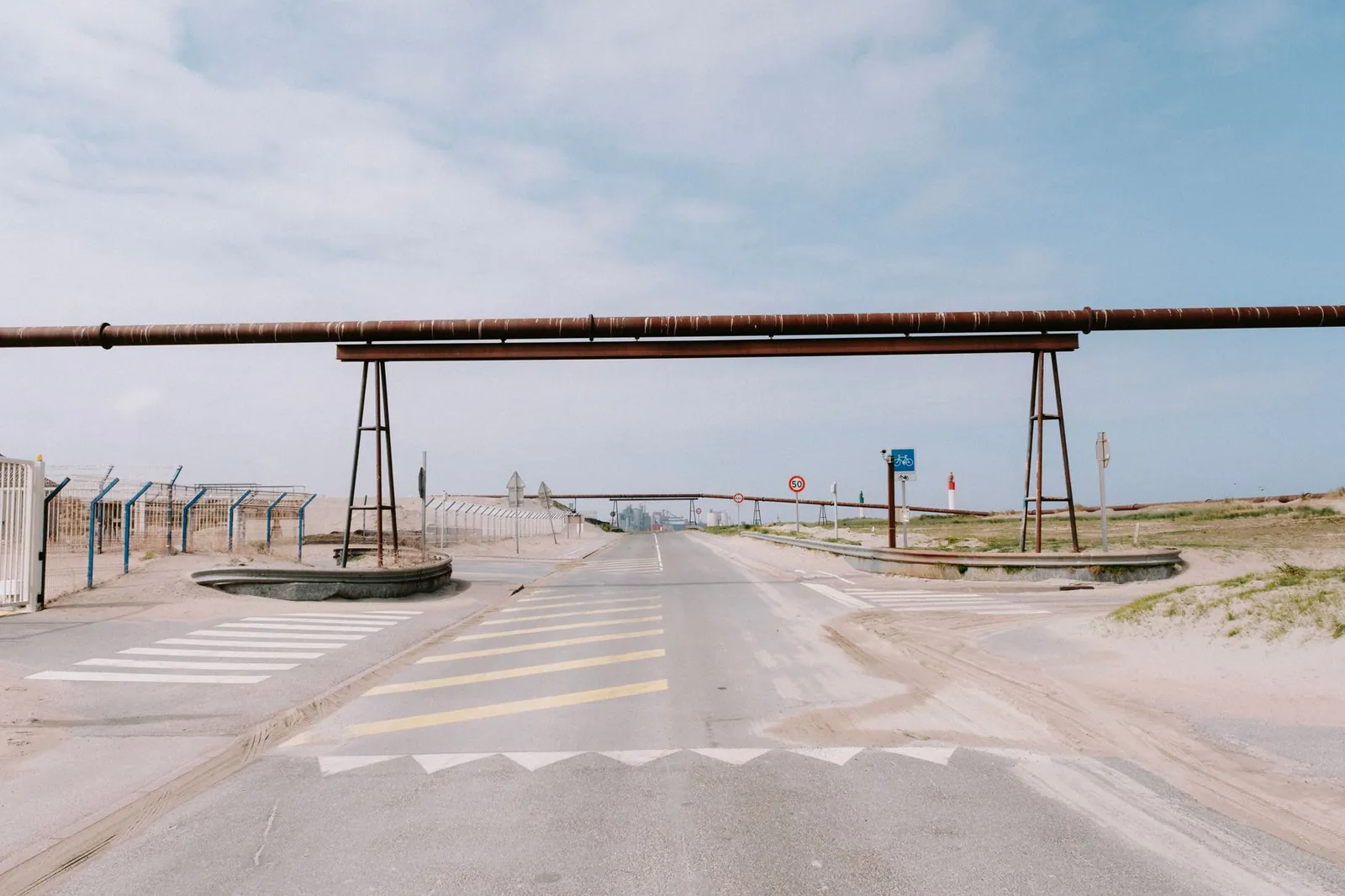 A coastal road featuring industrial pipelines, fences, and clear skies, ideal for industrial themes. Stock photo illustrating Man Industries (India)'s expansion story.