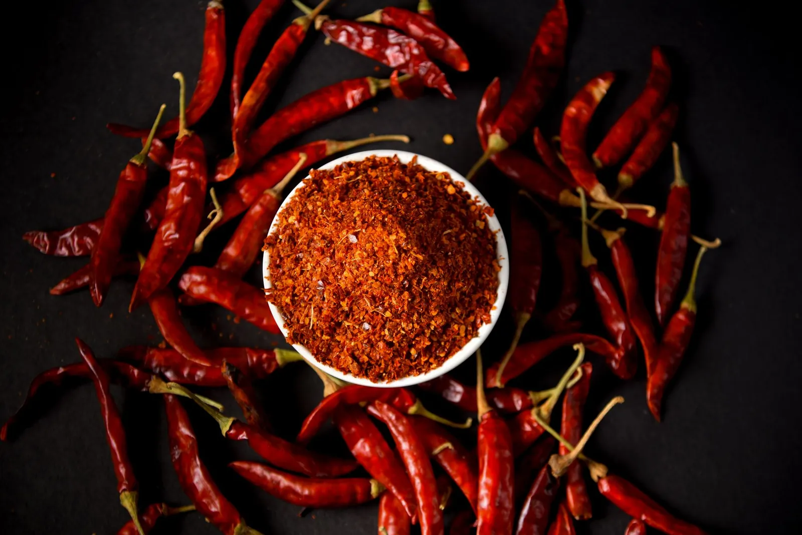 Red chili powder and whole chilies on dark background, showcasing spice and flavor. Stock photo illustrating Patel Retail's product launched story.