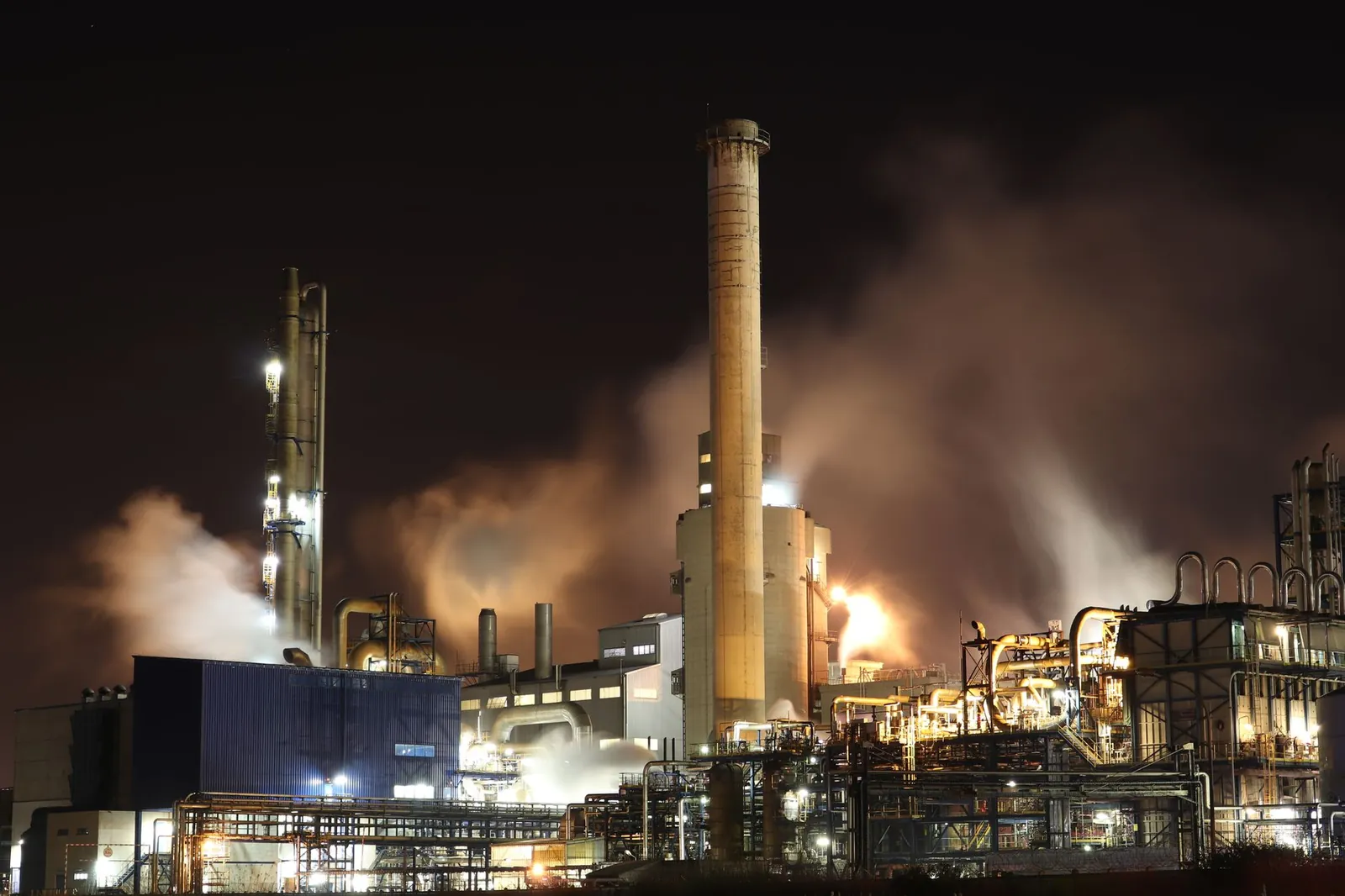 A nighttime view of an industrial factory with smokestacks emitting smoke, highlighting energy production and pollution. Stock photo illustrating Prasol Chemicals' financial results story.