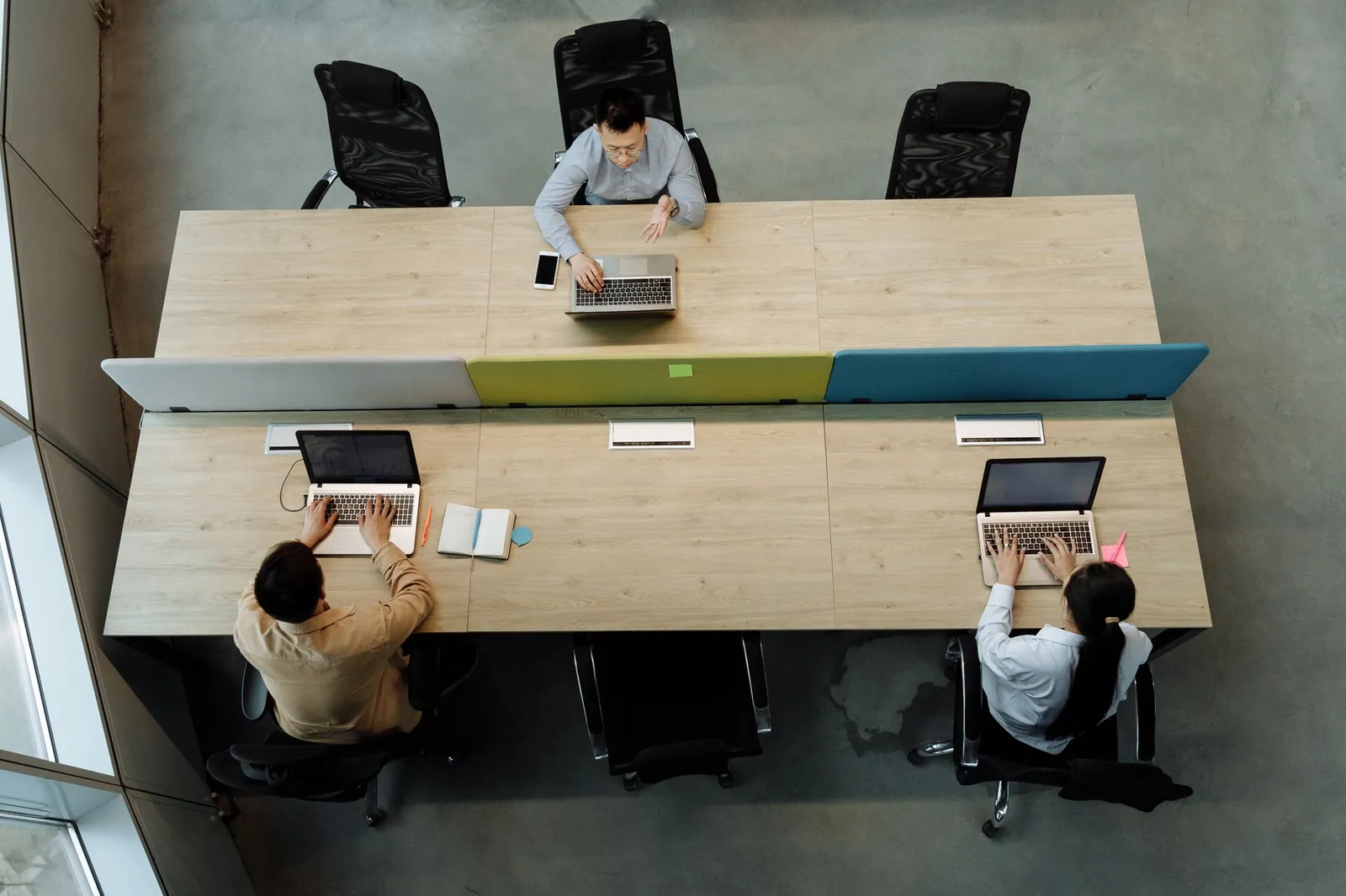 Three colleagues working at a shared office desk, using laptops in a modern workspace. Stock photo illustrating Smartworks Coworking Spaces' earning call story.