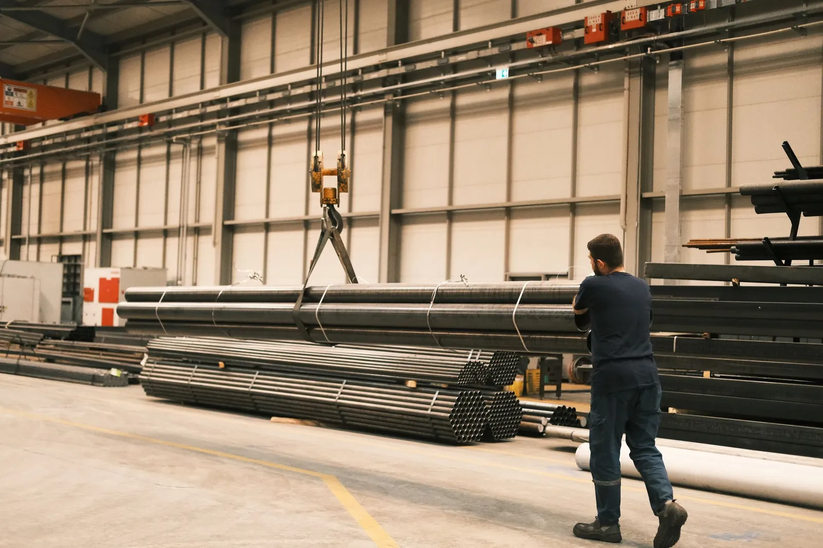 Steel pipes being maneuvered in an industrial facility by a worker using a crane. Stock photo illustrating Alliance Integrated Metaliks' fund raise story.