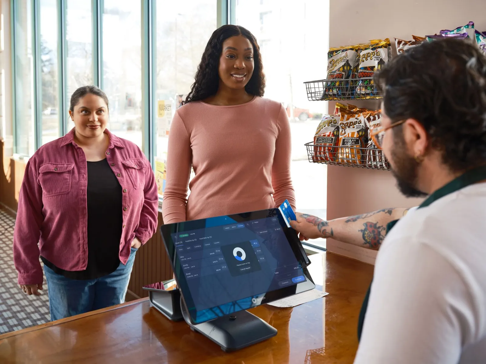 Two women making a payment at a convenience store using a touch screen POS system. Stock photo illustrating Network People Services Technologies' earning call story.