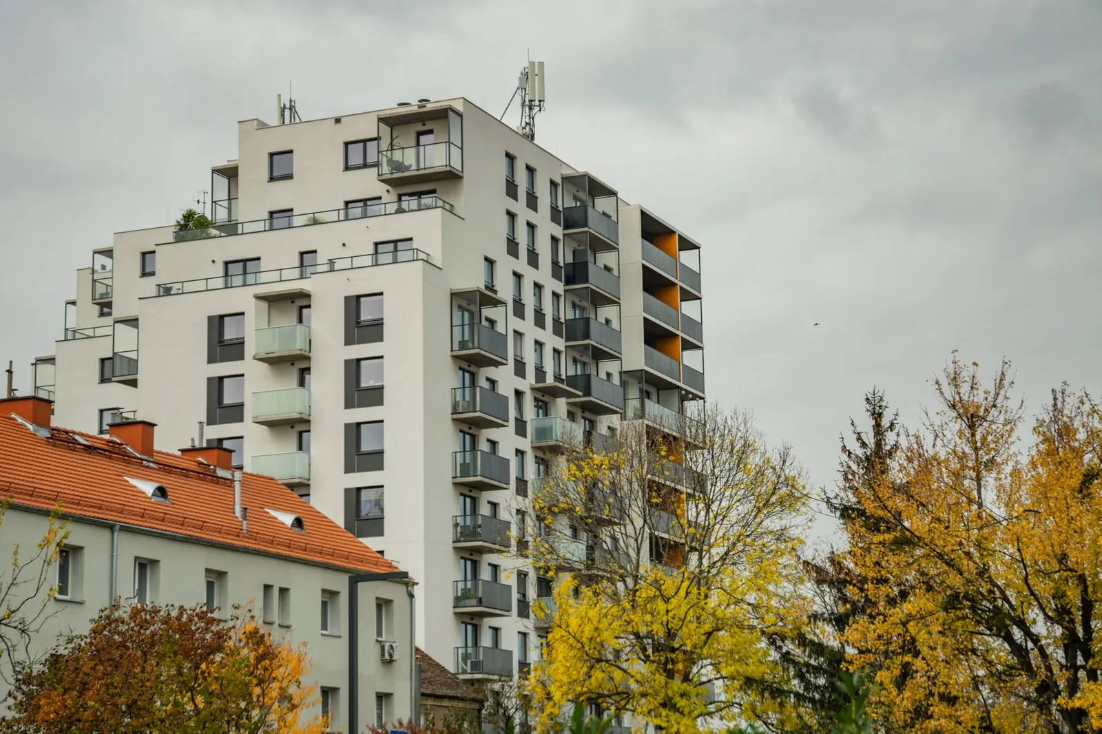 A modern apartment building surrounded by autumn trees under a cloudy sky. Stock photo illustrating Sri Lotus Developers and Realty's earning call story.