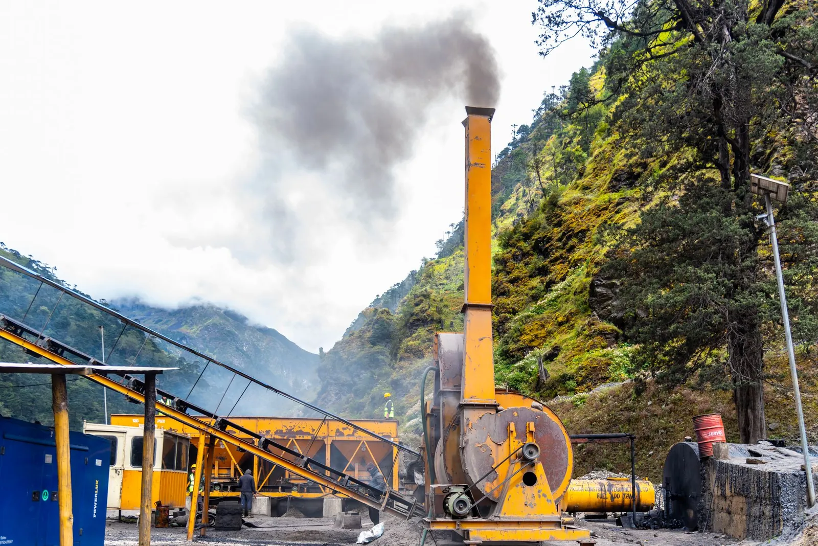 Industrial machinery emitting smoke in a scenic hilly area, showcasing construction activities in India. Stock photo illustrating Rbm Infracon's new order story.