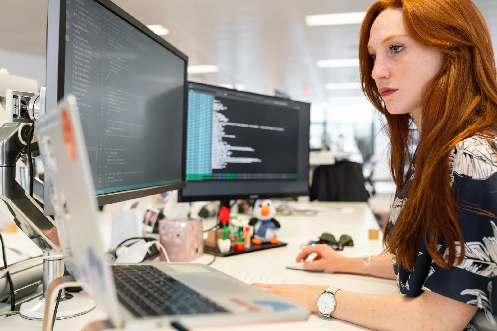 A focused female software engineer coding on dual monitors in a modern office. Stock photo illustrating Onward Technologies' earning call story.