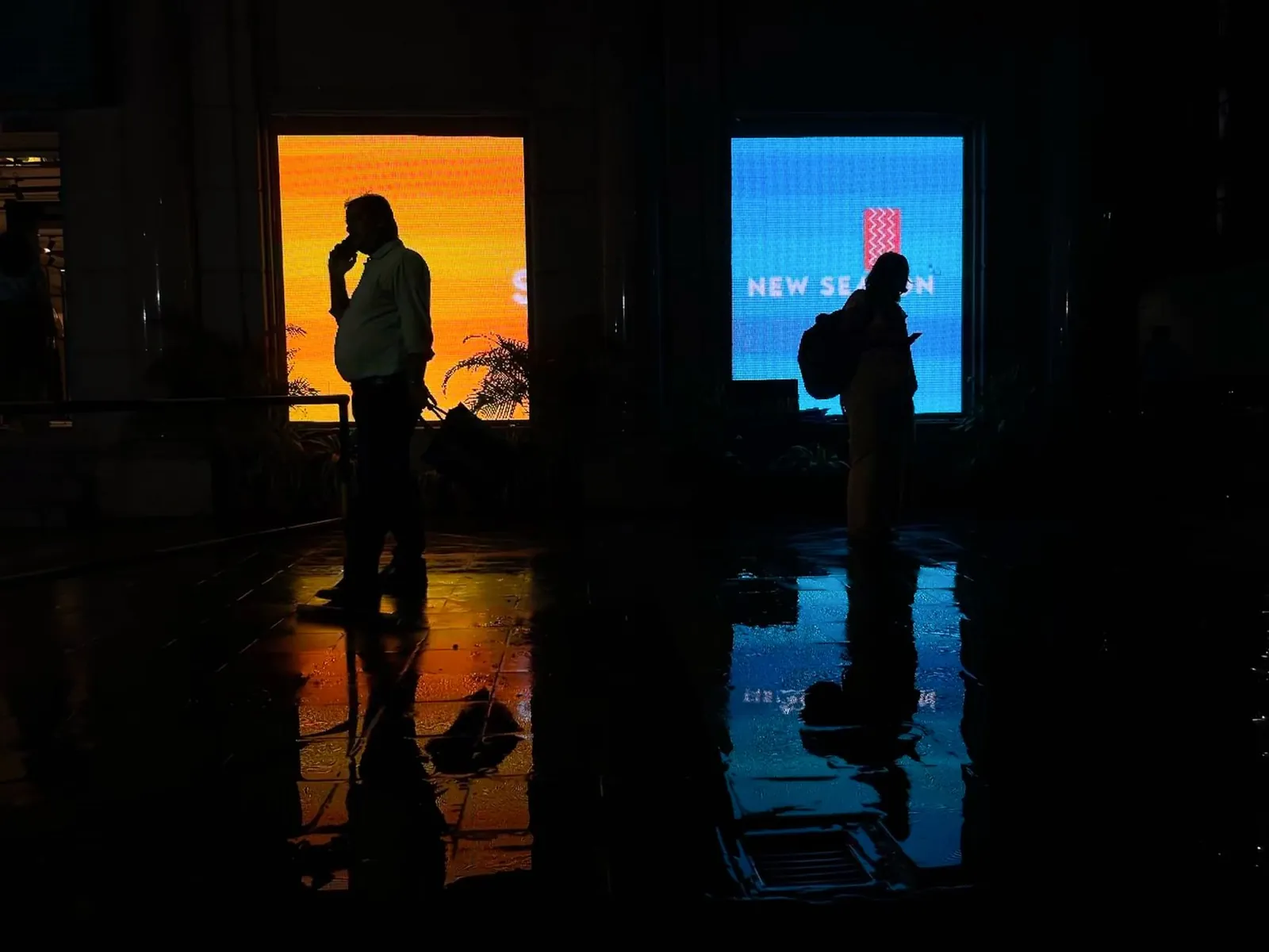 Two silhouettes in a dark corridor with vibrant billboard reflections creating a cinematic urban mood. Stock photo illustrating Simca Advertising's financial results story.