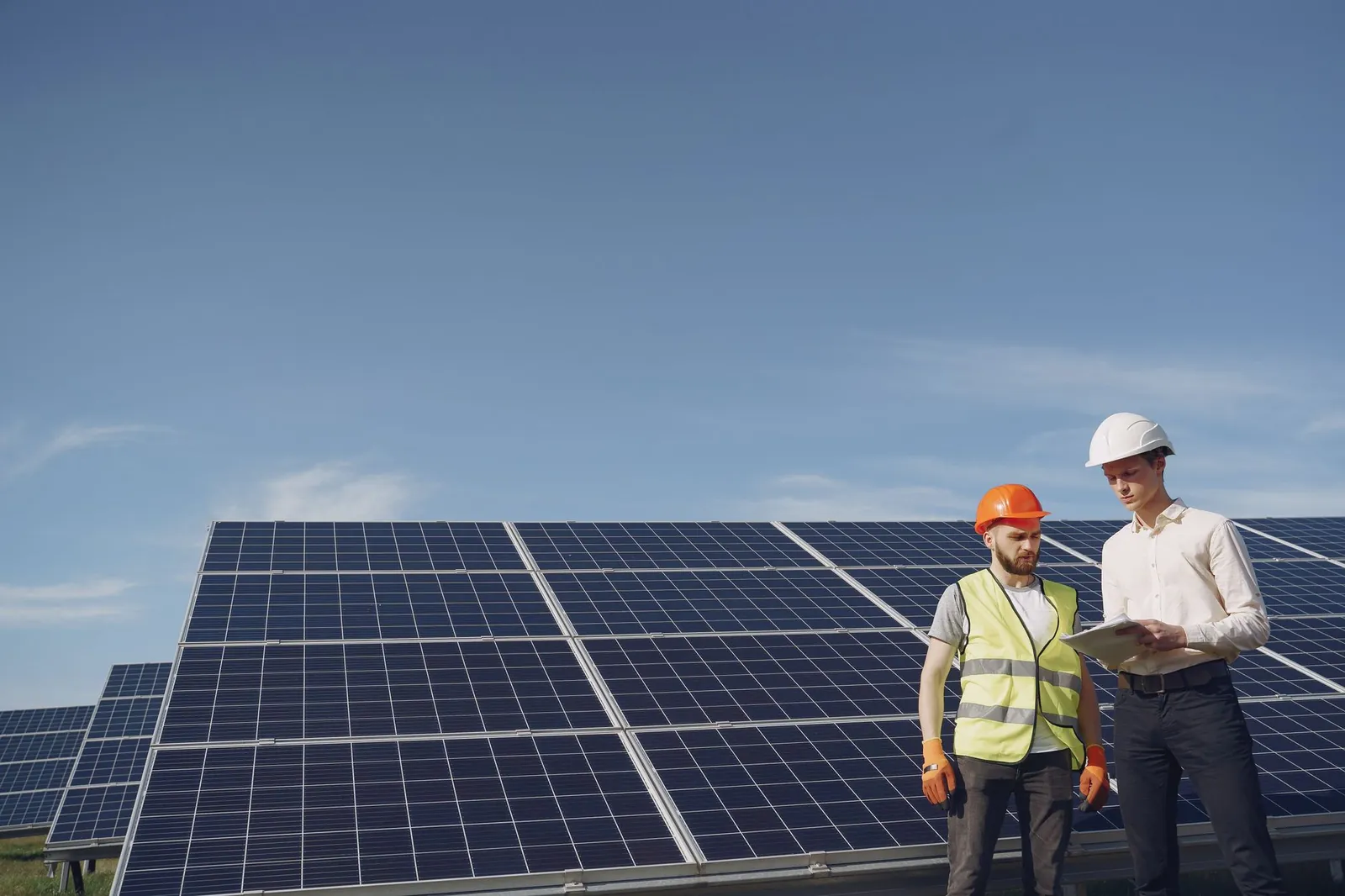 From below of serious young male colleagues in helmets working at solar energy station against cloudless blue sky. Stock photo illustrating Bondada Engineering's production started story.