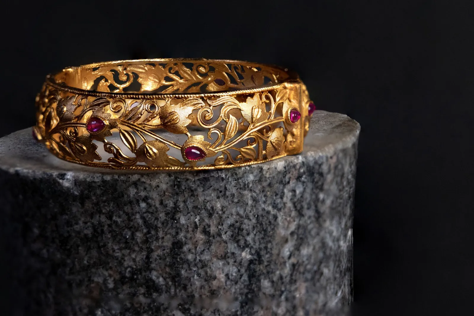 Intricate gold bracelet with ruby accents on a dark background. Luxurious and elegant design. Stock photo illustrating Motisons Jewellers' fund raise story.