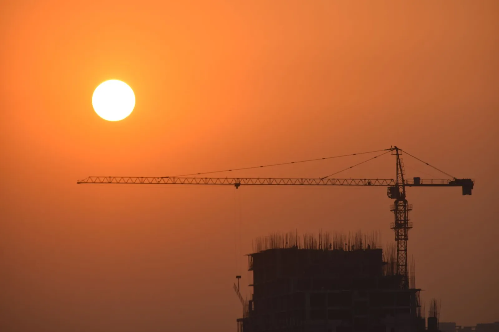 A striking silhouette of a construction crane set against a vibrant sunset sky in Faridabad, India. Stock photo illustrating Highway Infrastructure's earning call story.