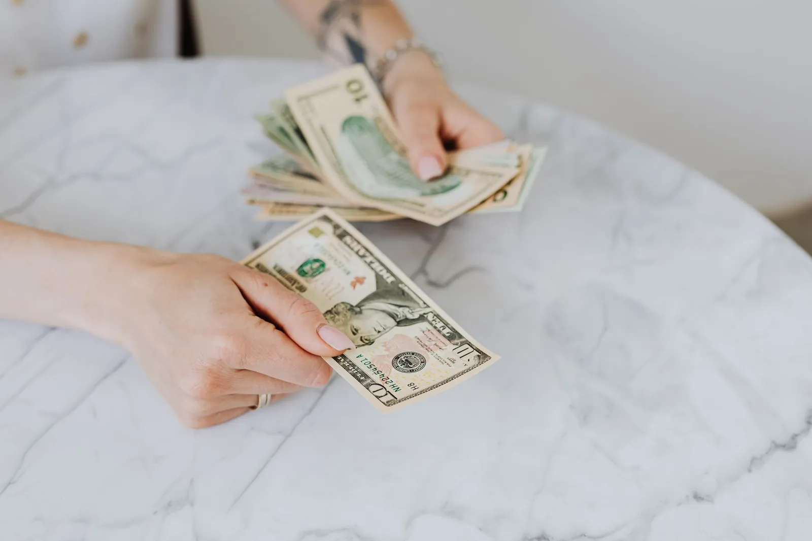 Close-up of hands counting US dollar bills on a marble table surface. Stock photo illustrating Capri Global Capital's expansion story.