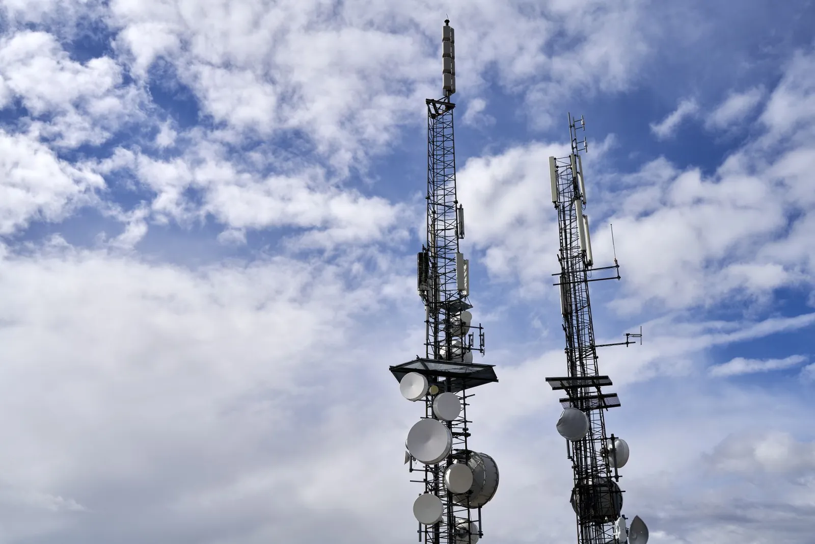 Telecommunication towers with antennas and dishes under a bright cloudy sky. Stock photo illustrating HEG Advanced Materials' partnership story.