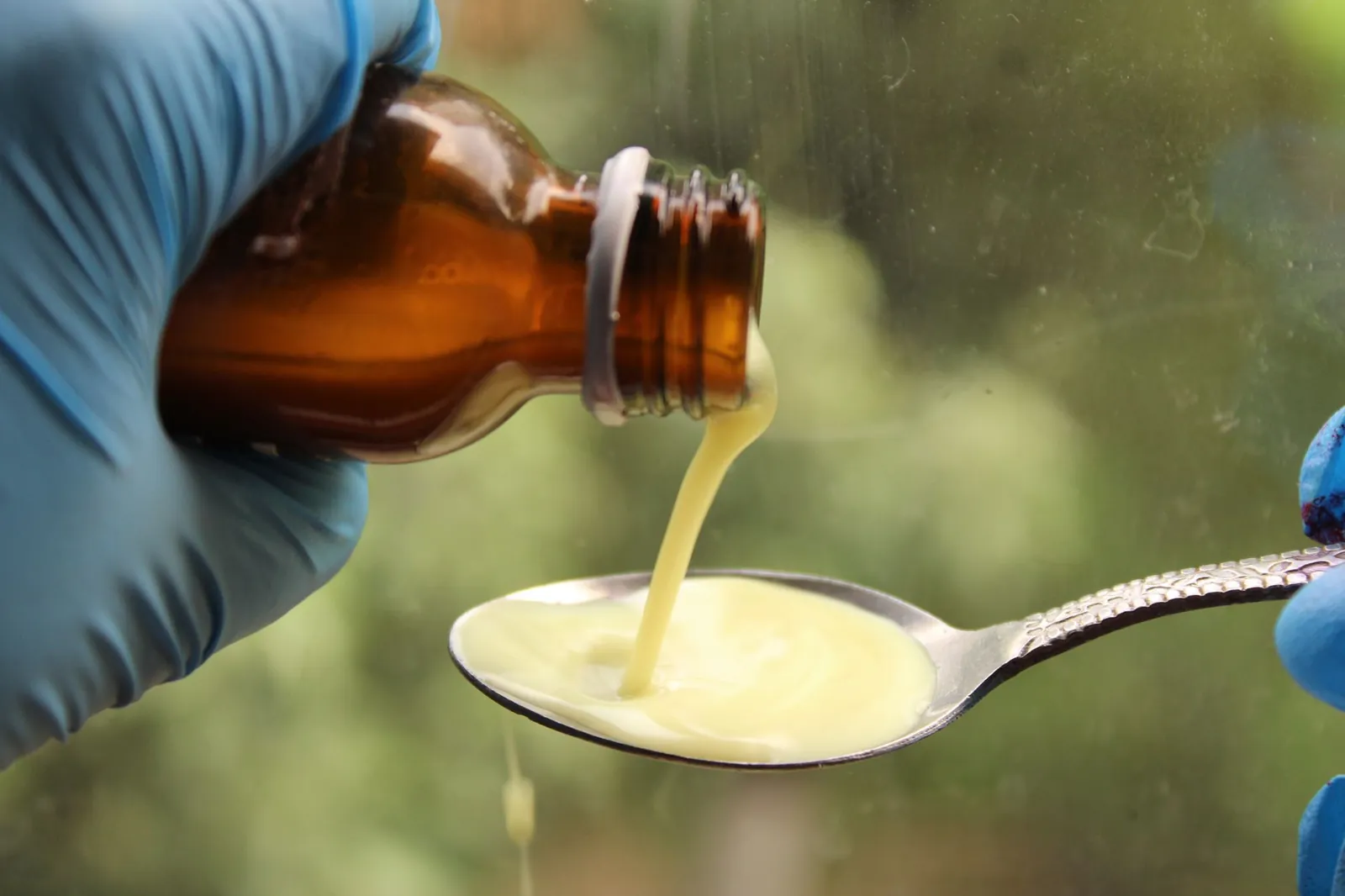 A gloved hand pours liquid medication from a brown bottle into a spoon. Stock photo illustrating Lupin's regulatory approval story.