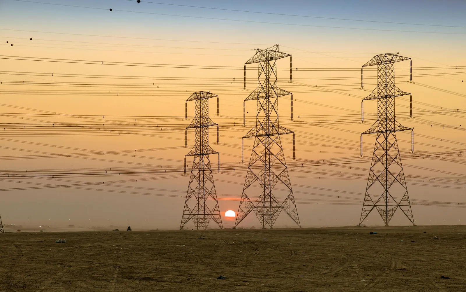 Three electricity pylons silhouetted against a vibrant sunset in open landscape. Stock photo illustrating Rajesh Power Services' new order story.