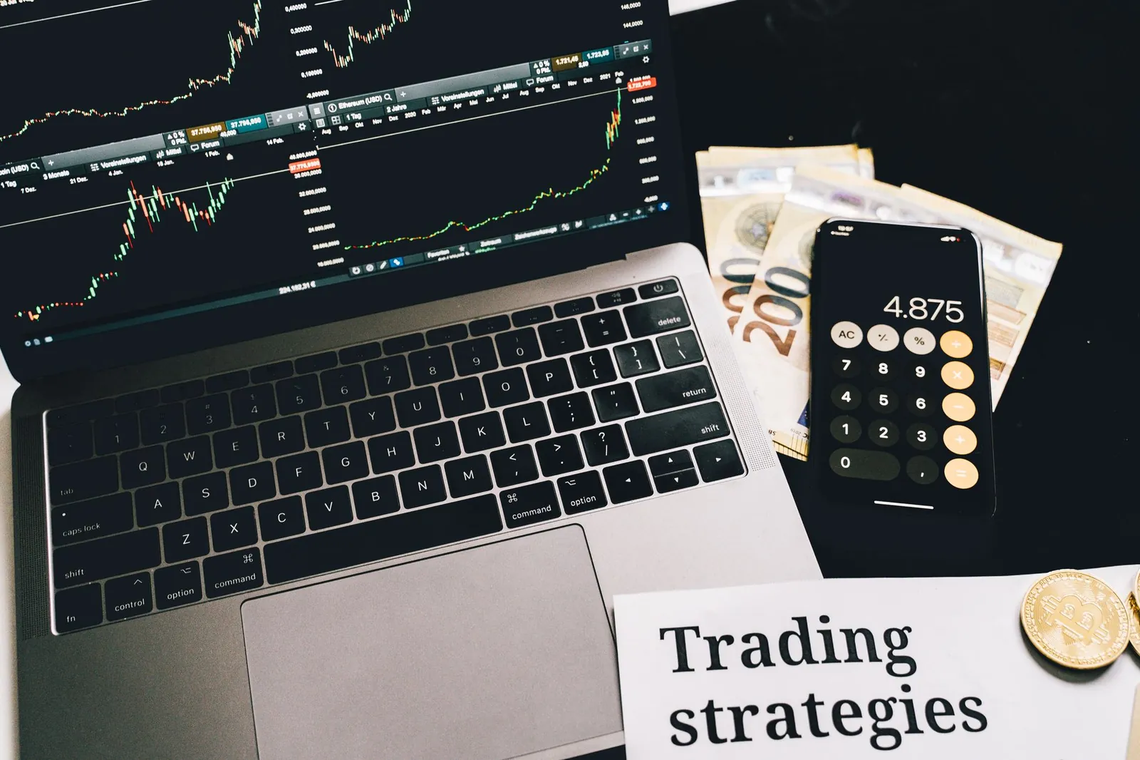 A laptop showing stock market graphs with a smartphone calculator, euro bills, coins, and trading strategies paper. Stock photo for the ALFA News guide: Trading Plans Under SEBI PIT Regulations: A Guide.