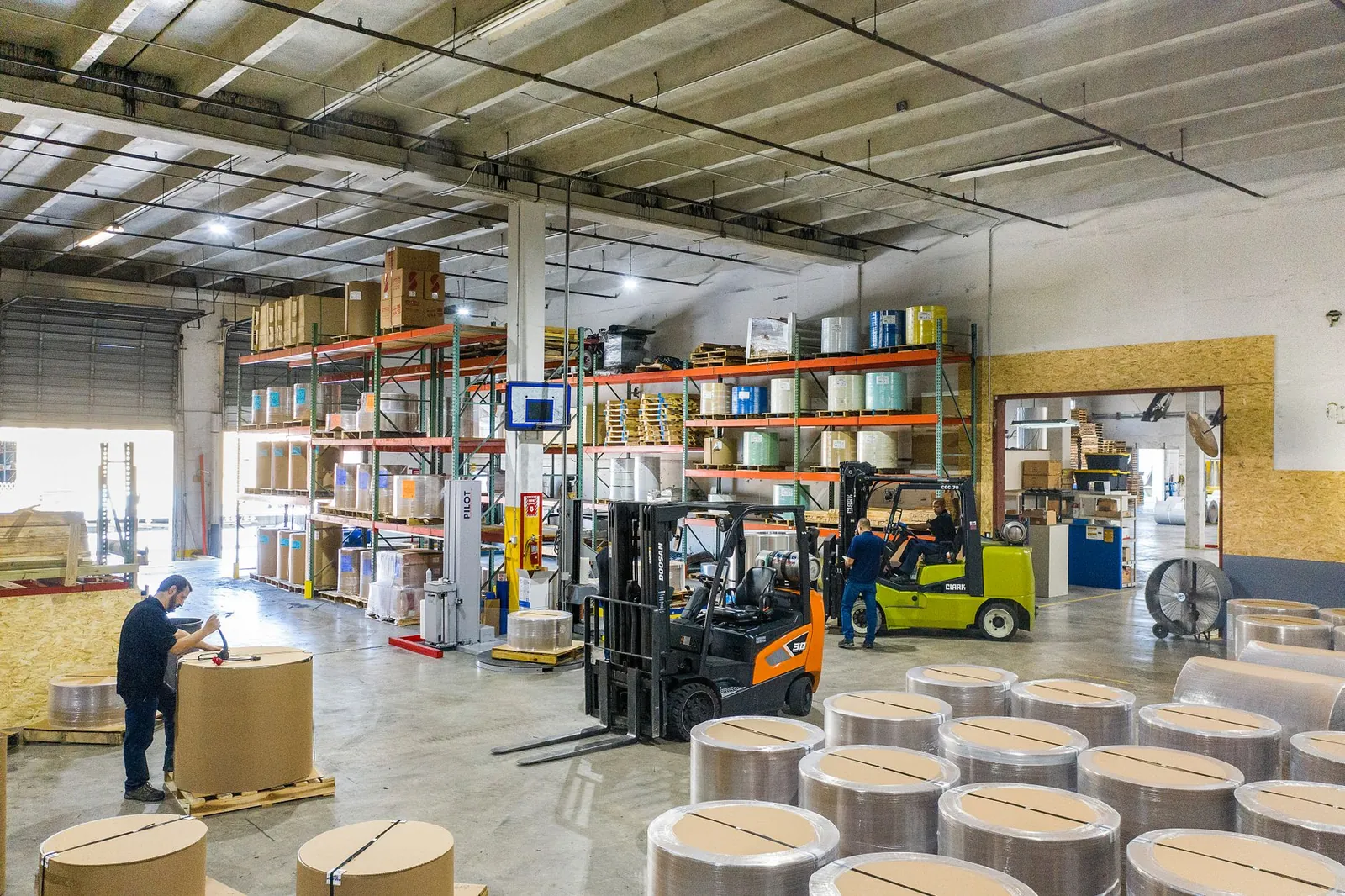 Interior view of a busy warehouse with forklifts and workers handling large rolls of material. Stock photo illustrating Emami Paper Mills' financial results story.