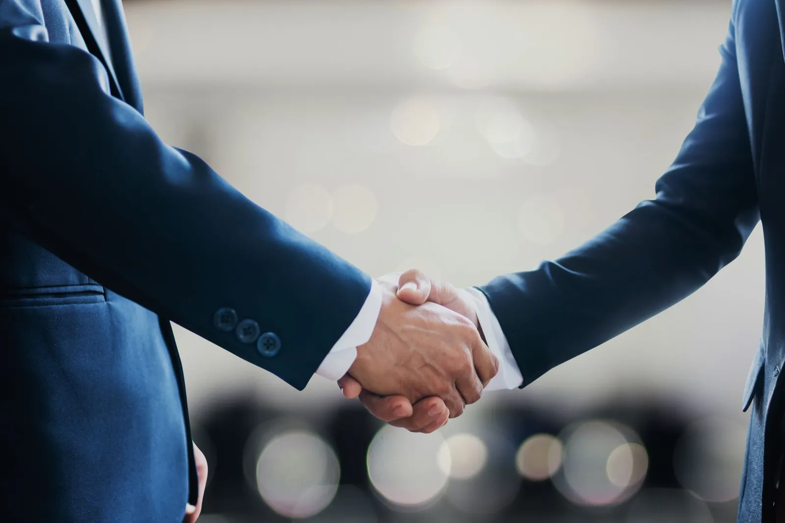 Close-up of business professionals in suits shaking hands, symbolizing a successful collaboration or agreement. Stock photo illustrating Exim Routes' partnership story.