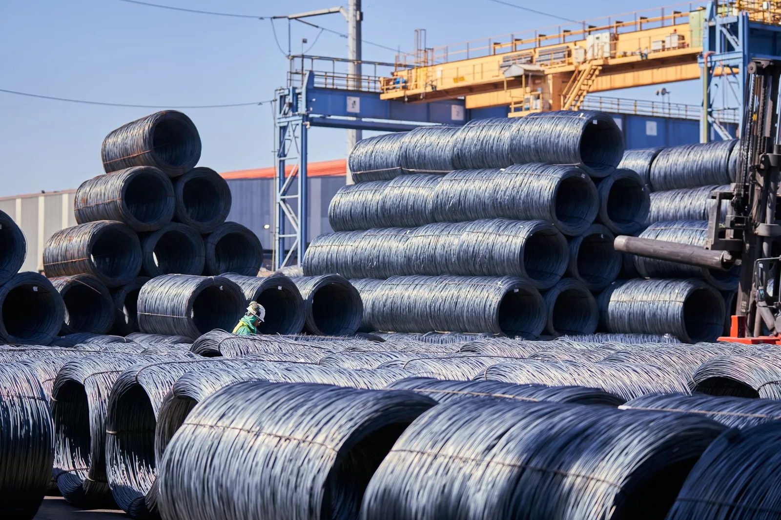 Large stacks of steel wire coils stored outdoors at an industrial site under bright daylight. Stock photo illustrating Jayesh Logistics' new order story.