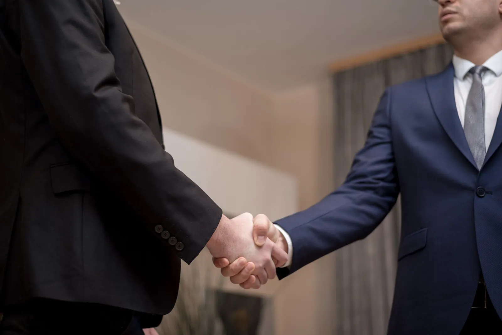 Two businessmen in suits shaking hands, emphasizing trust and partnership indoors. Stock photo illustrating Spice Lounge Food Works' partnership story.