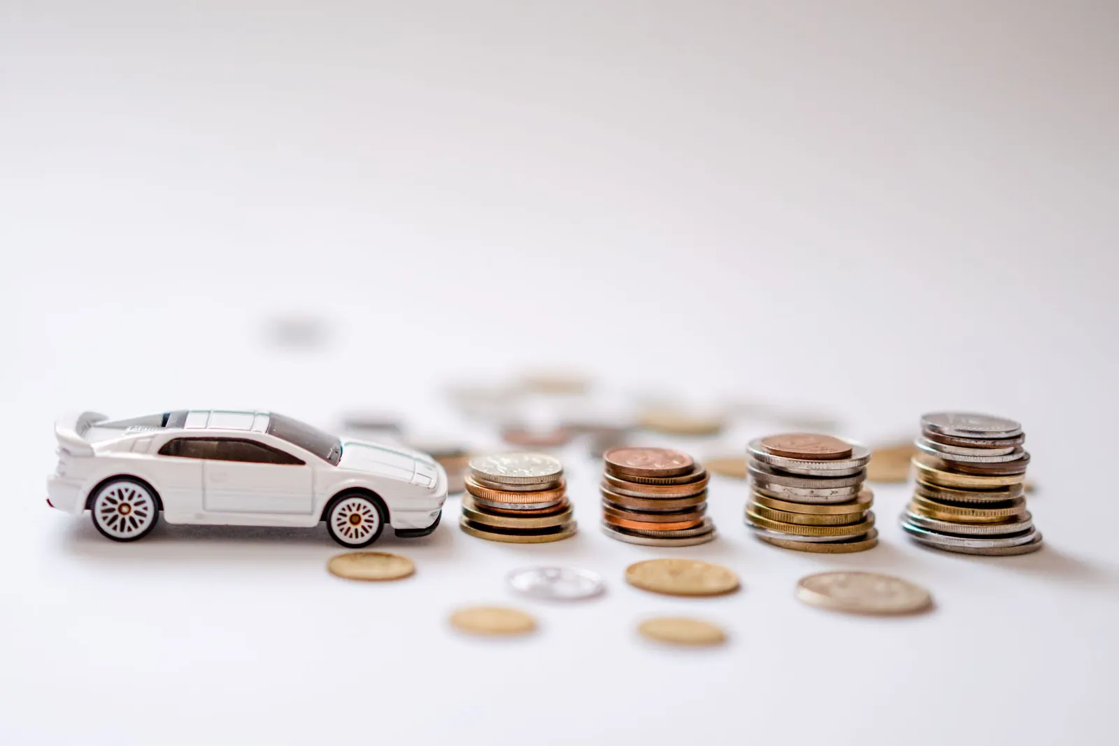 White toy sports car beside stacks of coins on a white background, emphasizing savings and finance. Stock photo illustrating AU Small Finance Bank's regulatory approval story.
