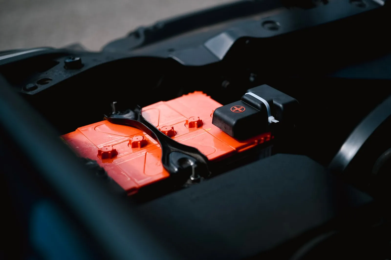Detailed view of an orange car battery inside a vehicle's engine bay, highlighting its features. Stock photo illustrating Bondada Engineering's new order story.